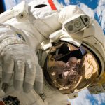 Space Technology - This picture shows an american astronaut in his space and extravehicular activity suite working outside of a spacecraft. In the background parts of a space shuttle are visible. In the far background of the picture planet earth with it's blue color and white clouds is shown as well as a patch of black space.