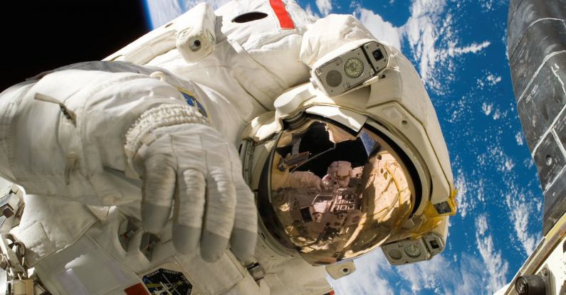 Space Technology - This picture shows an american astronaut in his space and extravehicular activity suite working outside of a spacecraft. In the background parts of a space shuttle are visible. In the far background of the picture planet earth with it's blue color and white clouds is shown as well as a patch of black space.