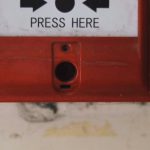 Spyware Detection - Manual emergency red fire alarm system box with push button placed on white shabby wall in light room of building