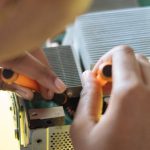 Gadget Maintenance - Crop of ethnic system administrator in uniform using screwdrivers and checking motherboard on electronic equipment during work in repair department